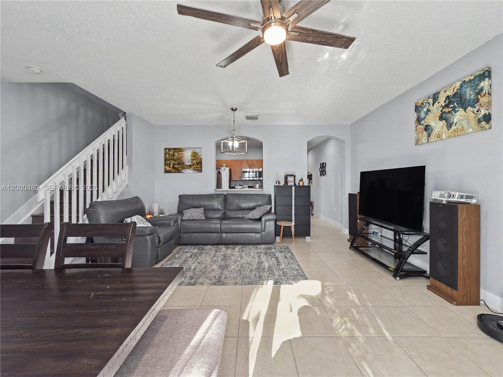 A living room features a grey sofa, a television, and a staircase with white railings — 1033 NE 42nd Pl, Homestead FL 33033, HOMESTEAD, FL