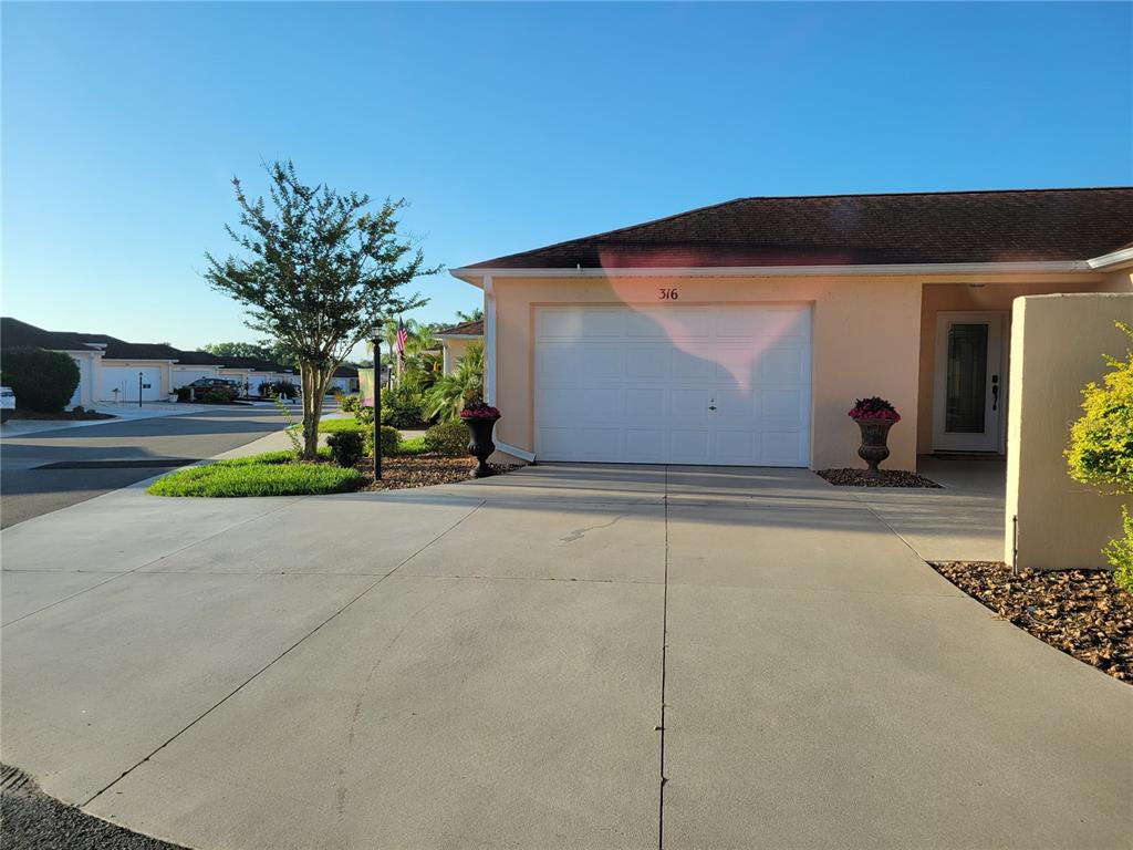 A single-story house with a white garage door, concrete driveway, and light-colored exterior walls — 316 GUIDO AVENUE, LADY LAKE, FL