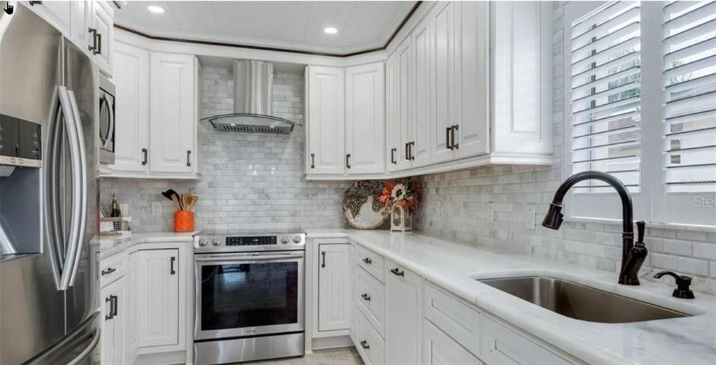 A kitchen features white cabinets, stainless steel appliances, marble countertops, and a subway tile backsplash — 316 GUIDO AVENUE, LADY LAKE, FL