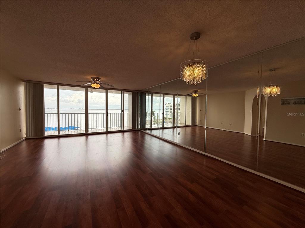 A living room with wood flooring, mirrored walls, a crystal chandelier, and a balcony view — 5155 ISLA KEY BOULEVARD S UNIT 307, ST PETERSBURG, FL