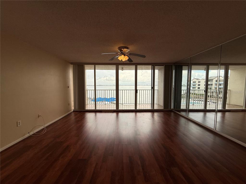 An empty living room features dark wood flooring, a ceiling fan, and a glass balcony door — 5155 ISLA KEY BOULEVARD S UNIT 307, ST PETERSBURG, FL