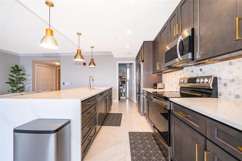 A modern kitchen features dark cabinetry, white quartz countertops, stainless steel appliances, and pendant lighting — 16300 COUNTY ROAD 455 UNIT 602, MONTVERDE, FL