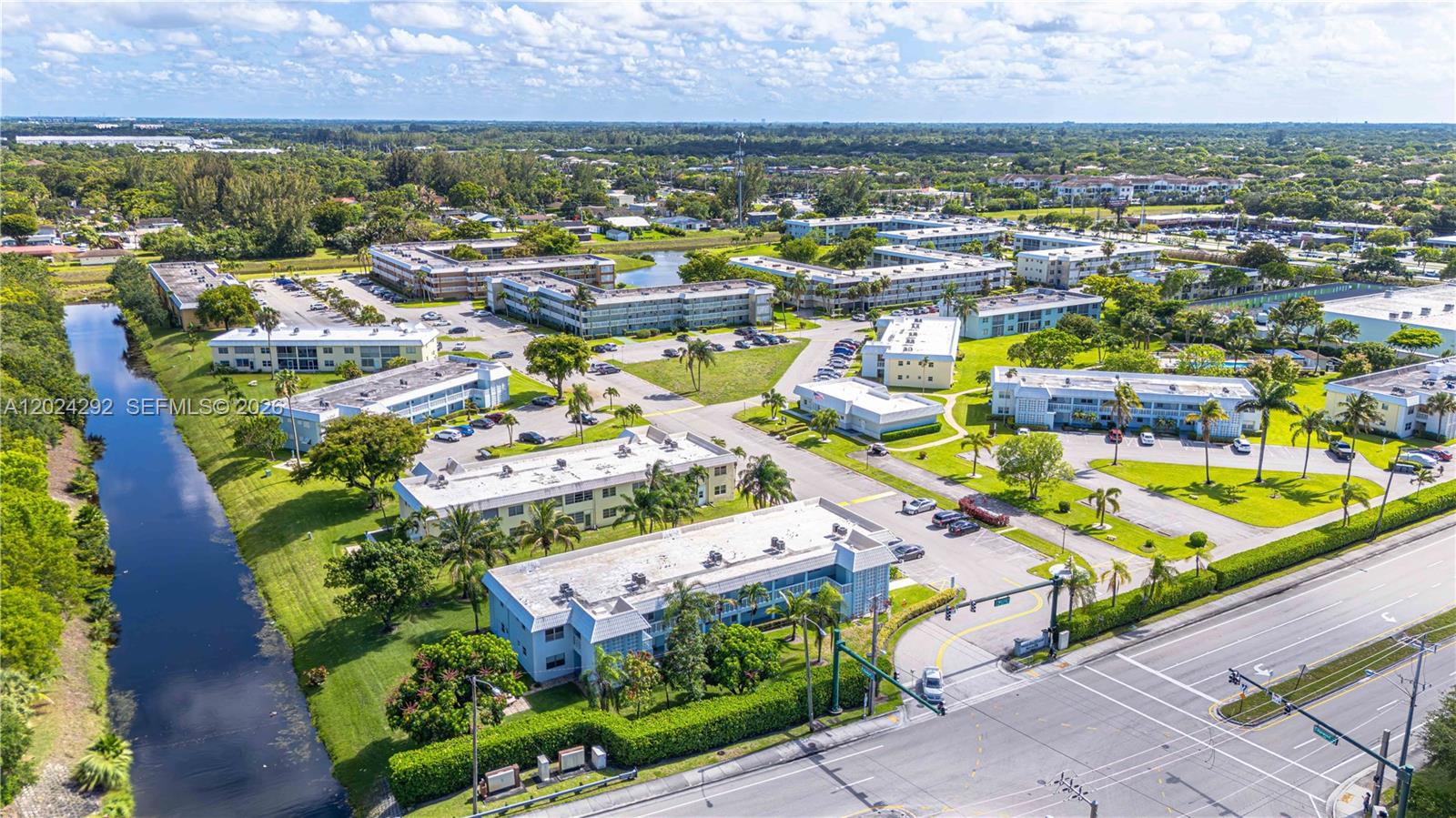 An aerial view shows a multi-building apartment complex with a canal and surrounding greenery — 9780 N Marina Blvd # 424, Boca Raton FL 33428, BOCA RATON, FL