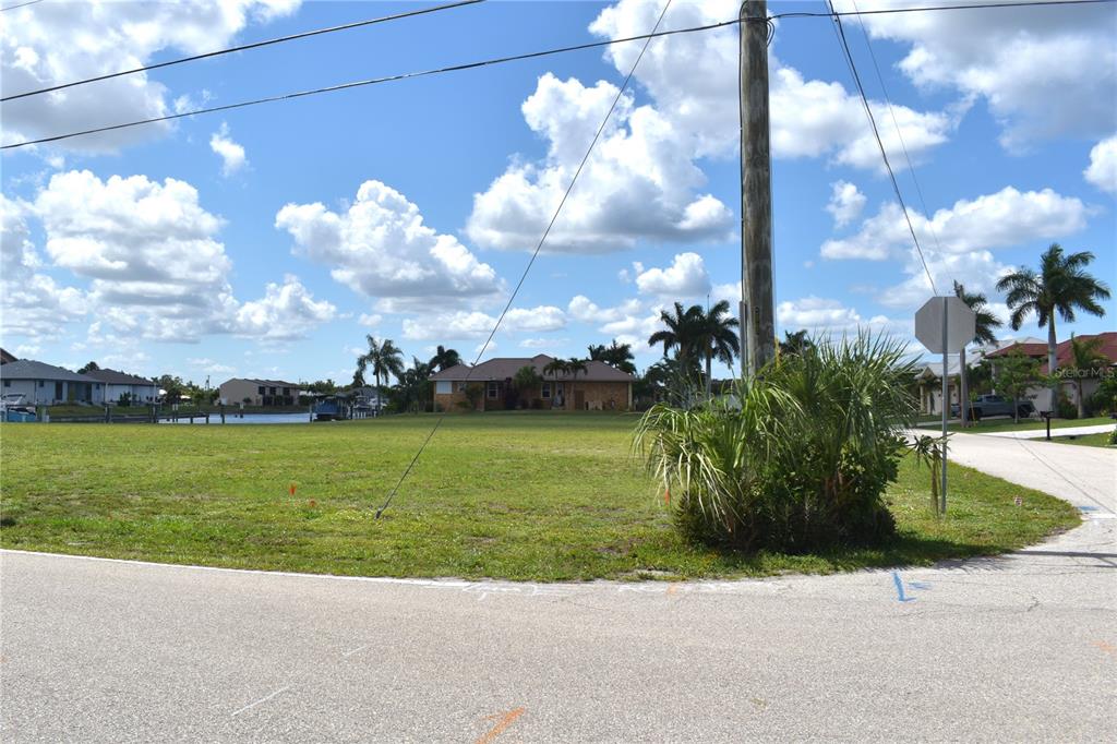 A vacant grassy lot sits along a canal with palm trees and houses in the background — 825 VIA TRIPOLI, PUNTA GORDA, FL