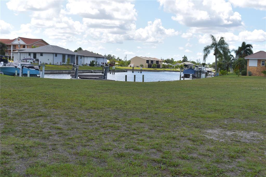 A grassy lot overlooks a canal with boat docks and residential houses in the background — 825 VIA TRIPOLI, PUNTA GORDA, FL