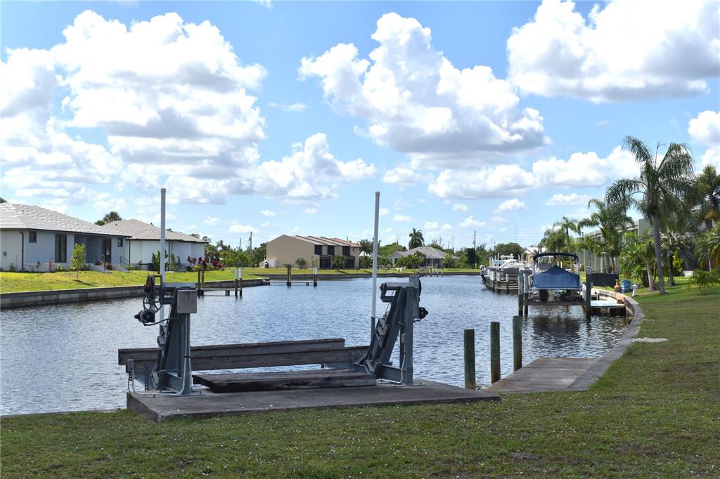 A boat lift sits on a concrete pad along a residential canal with docked boats — 825 VIA TRIPOLI, PUNTA GORDA, FL