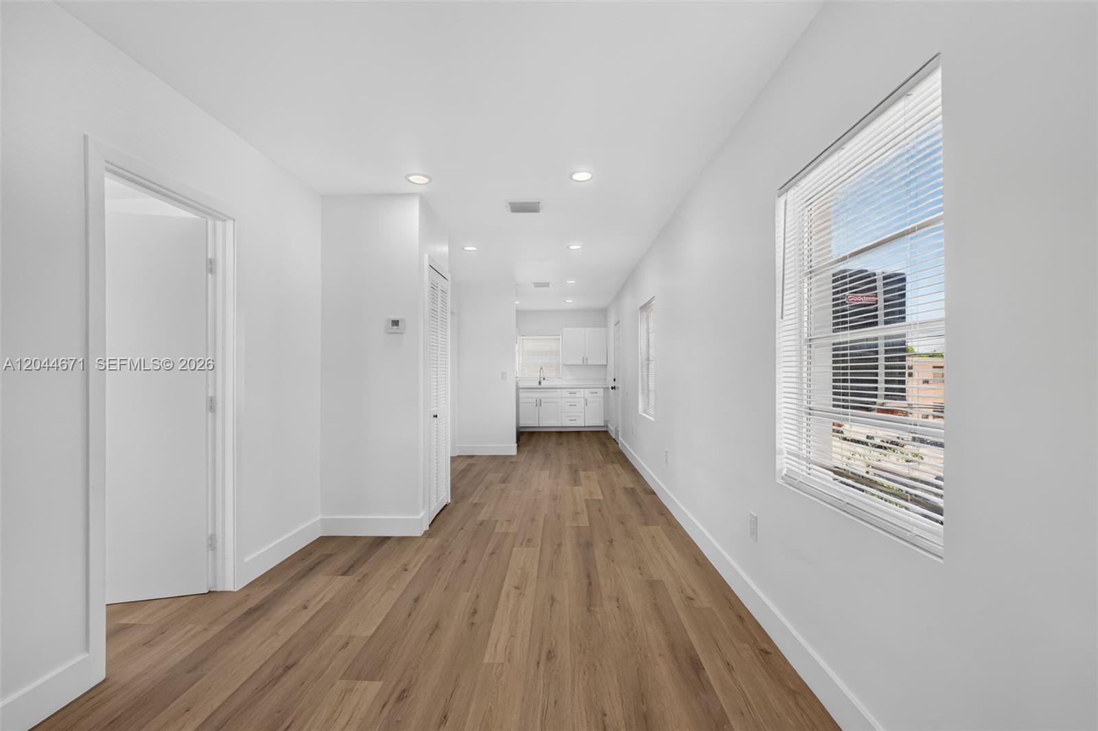 A bright, empty room with wood-look flooring leads to a kitchen with white cabinets — 1900 SW 6th St SW 6th St # 6, Miami FL 33135, MIAMI, FL