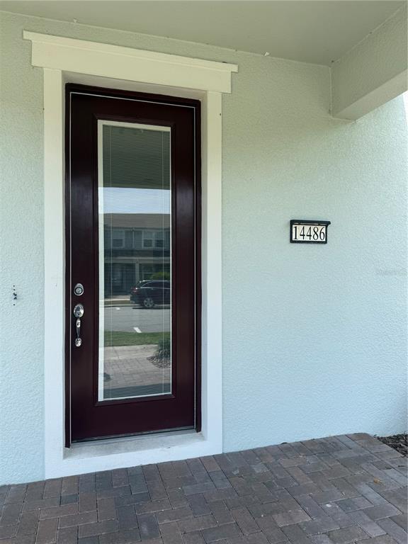 A dark red front door with a glass insert sits beside a house number plaque — 14486 SAPELO BEACH DRIVE, ORLANDO, FL