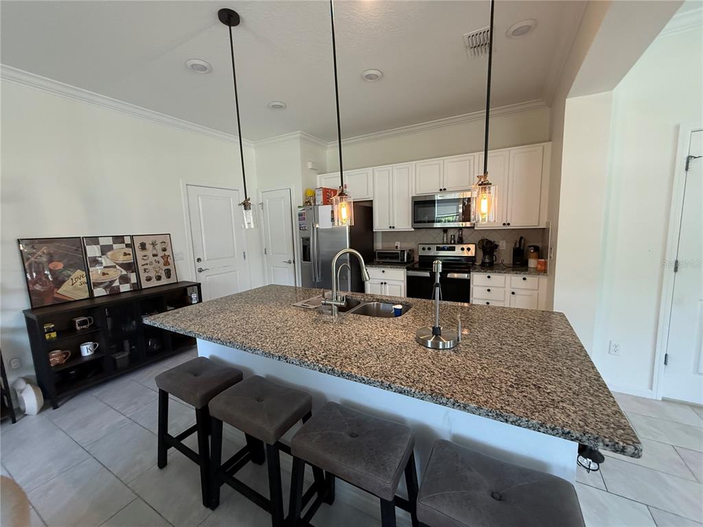 A kitchen features a granite-topped island with bar stools, white cabinetry, and stainless steel appliances — 14486 SAPELO BEACH DRIVE, ORLANDO, FL