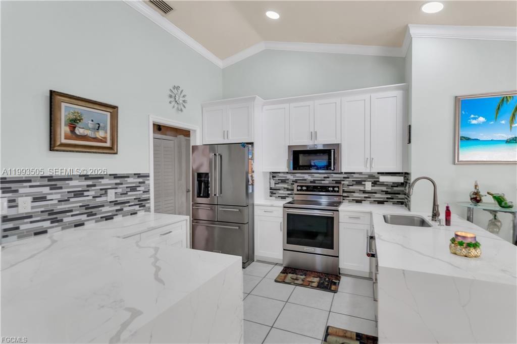 A kitchen features white cabinets, stainless steel appliances, a tiled backsplash, and white countertops — 2504 E 7th ST, Lehigh Acres FL 33936, LEHIGH ACRES, FL
