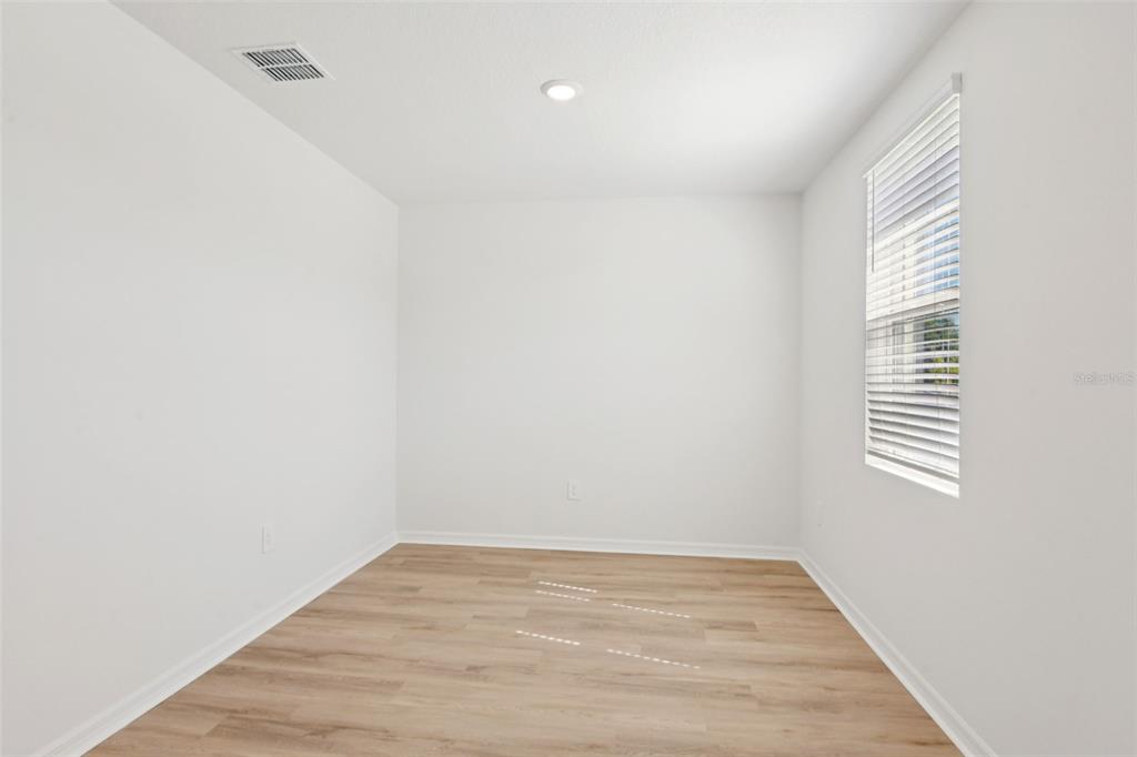 An empty room with white walls, light wood-look flooring, and a window with blinds — 12597 HOMELAND DRIVE, DADE CITY, FL