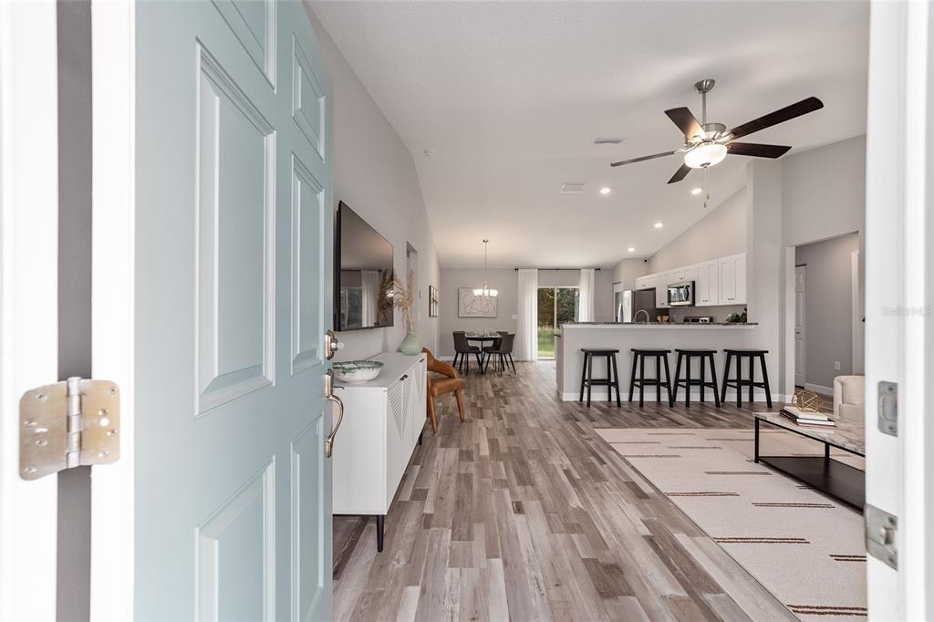 A view from an open doorway into a living room with wood-look flooring and kitchen — 8 Dogwood TRAIL TERRACE, OCALA, FL