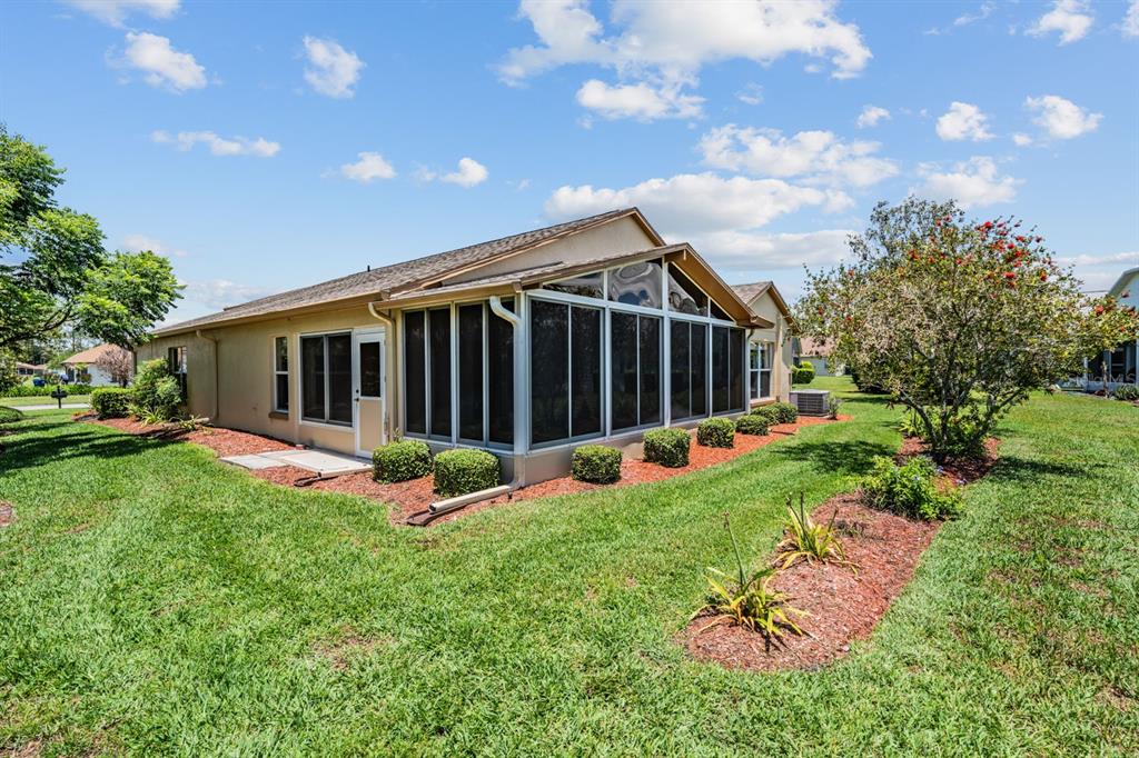 The exterior of a tan house features a screened-in porch and a landscaped yard — 11709 SPINDRIFT LOOP, HUDSON, FL