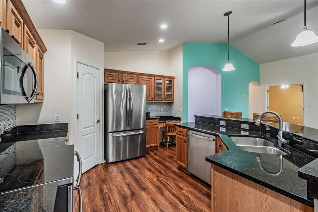 A kitchen features stainless steel appliances, dark granite countertops, wood cabinets, and wood-look flooring — 11709 SPINDRIFT LOOP, HUDSON, FL