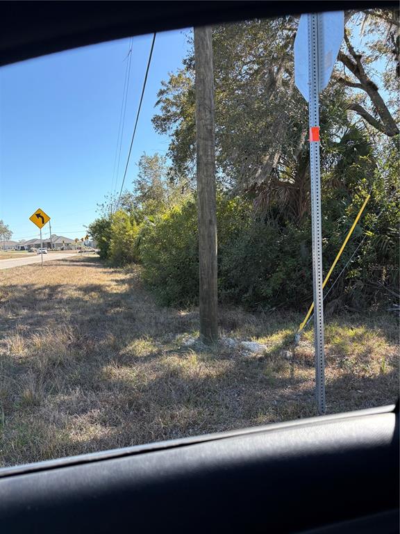 A utility pole stands in a grassy, wooded lot next to a road with signage — 2049 CORNELIUS BOULEVARD, PORT CHARLOTTE, FL
