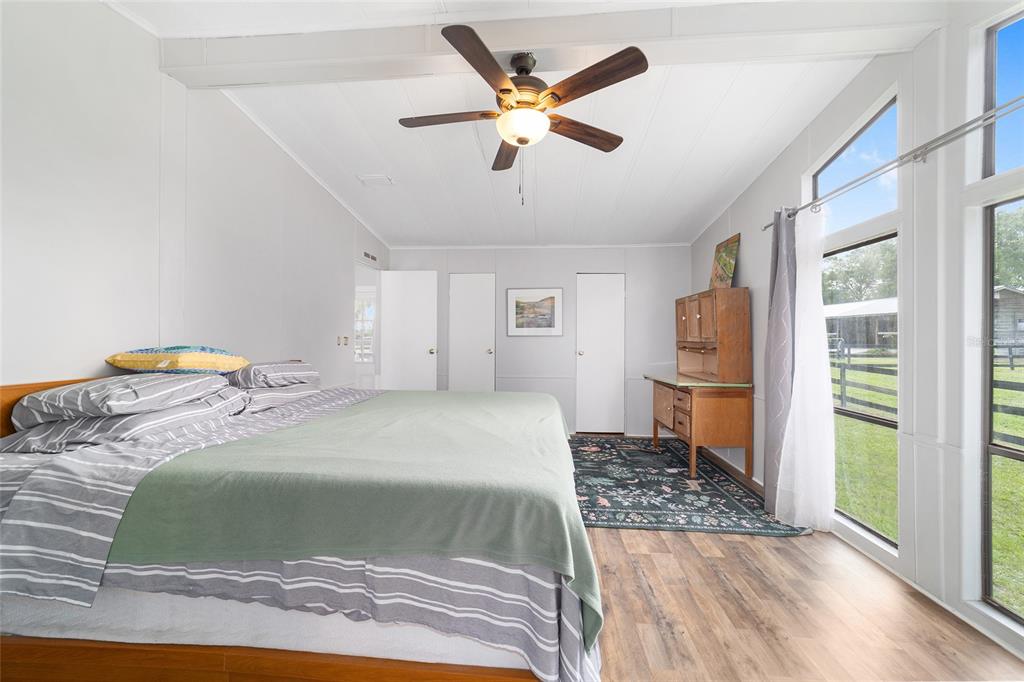 A bedroom with a large bed, wood-look flooring, a ceiling fan, and floor-to-ceiling windows — 3371 NW 120TH AVENUE, OCALA, FL