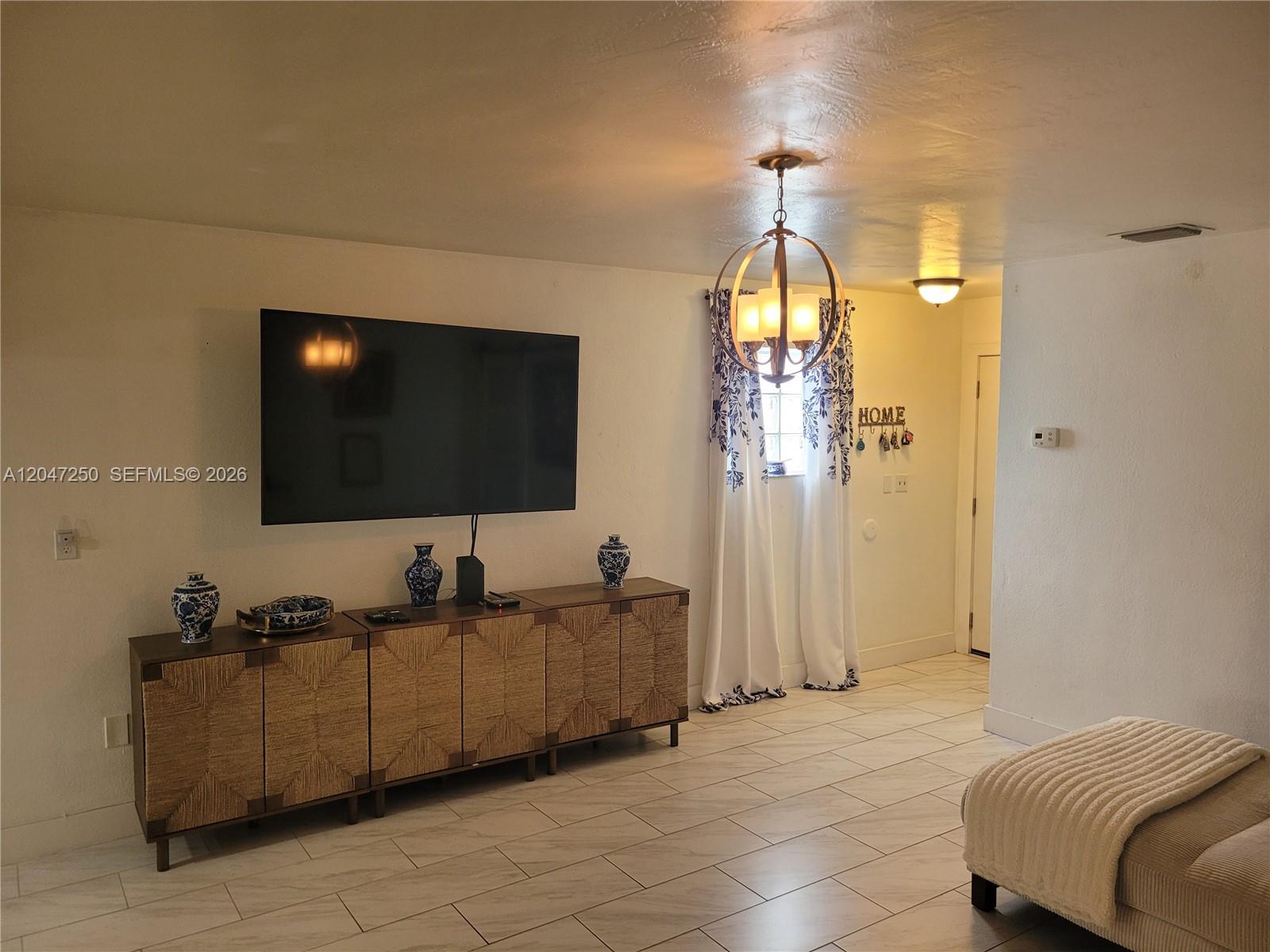 A living room features a wall-mounted television, a textured sideboard, and a spherical chandelier — 6691 W 15th Ct # 1, Hialeah FL 33012, HIALEAH, FL