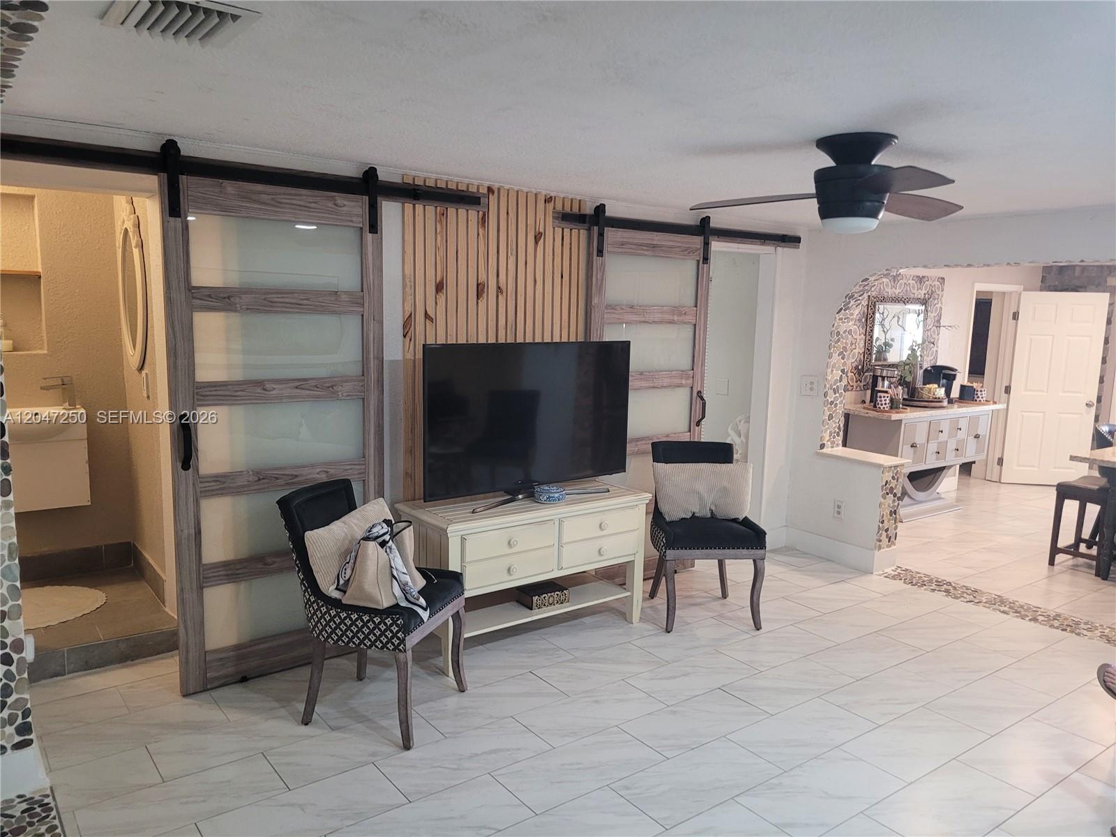 A living room features a television on a console between two sliding glass barn doors — 6691 W 15th Ct # 1, Hialeah FL 33012, HIALEAH, FL