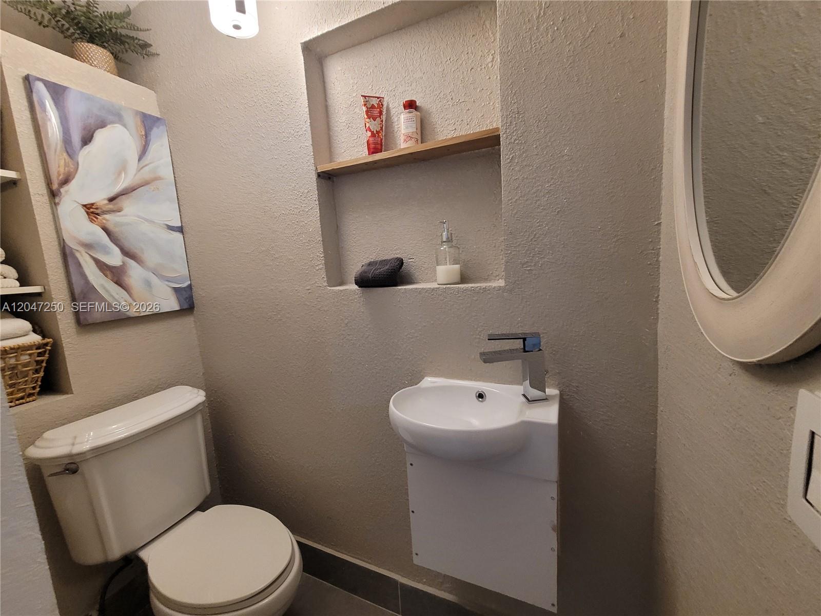 A small bathroom features a wall-mounted sink, a toilet, and a recessed wall shelf — 6691 W 15th Ct # 1, Hialeah FL 33012, HIALEAH, FL