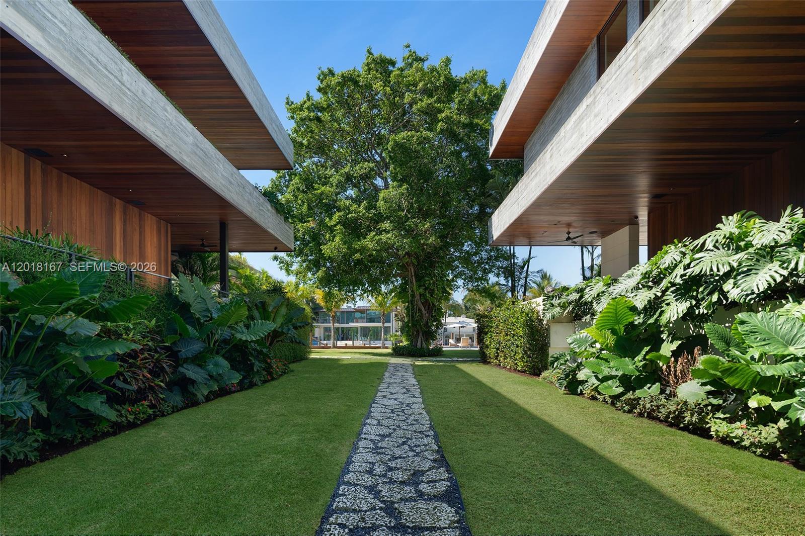 A stone path leads between two modern buildings with wood-paneled ceilings toward a large tree — 1420 W 23rd St, Miami Beach FL 33140, MIAMI BEACH, FL