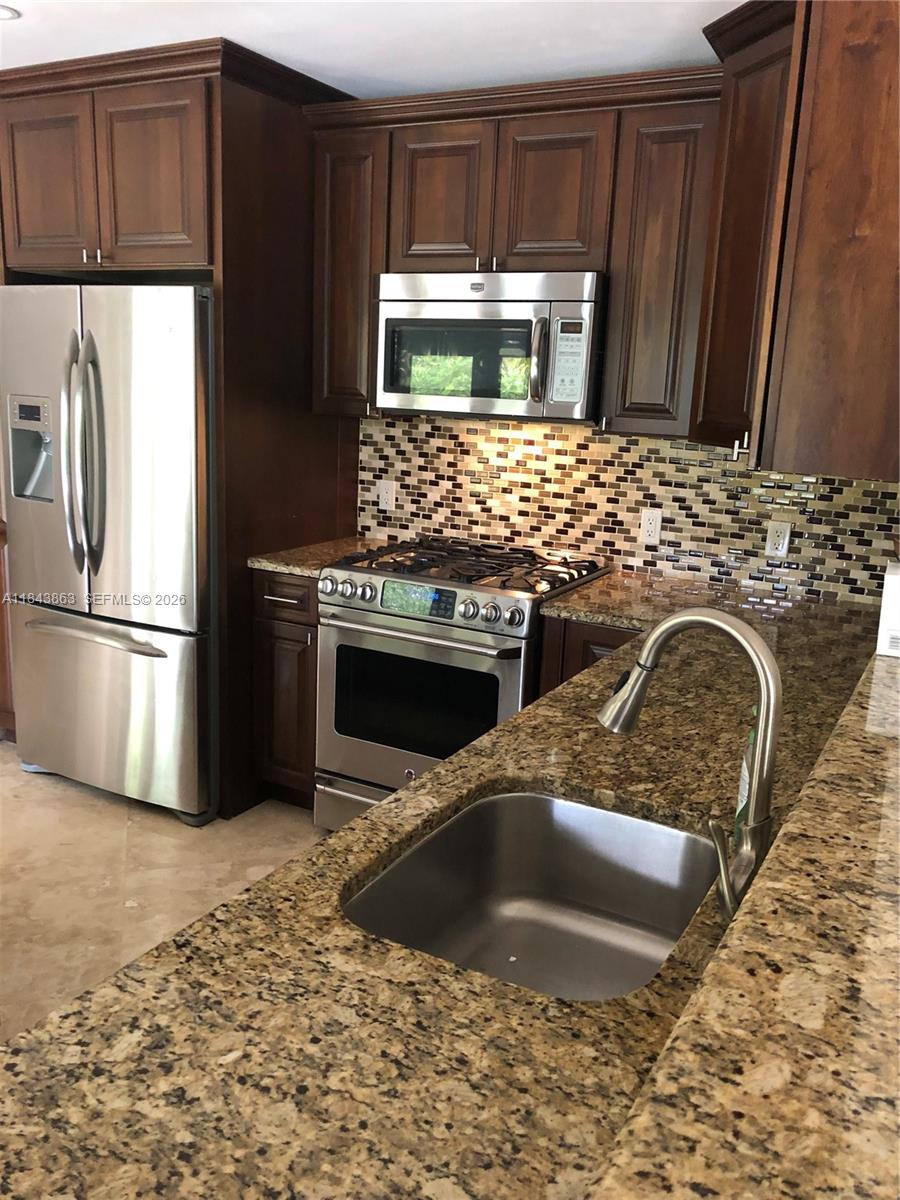 A kitchen features dark wood cabinets, granite countertops, stainless steel appliances, and a mosaic backsplash — 10801 SW 123rd St, Miami FL 33176, MIAMI, FL