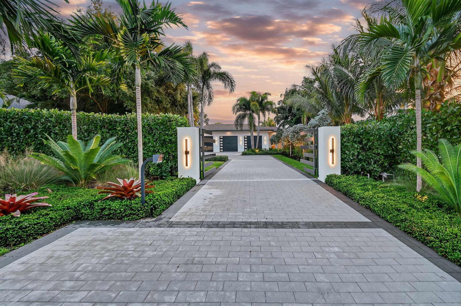 A paved driveway leads through a gated entrance toward a modern house surrounded by palm trees — 2085 Vitex Lane, North Palm Beach FL 33408, NORTH PALM BEACH, FL