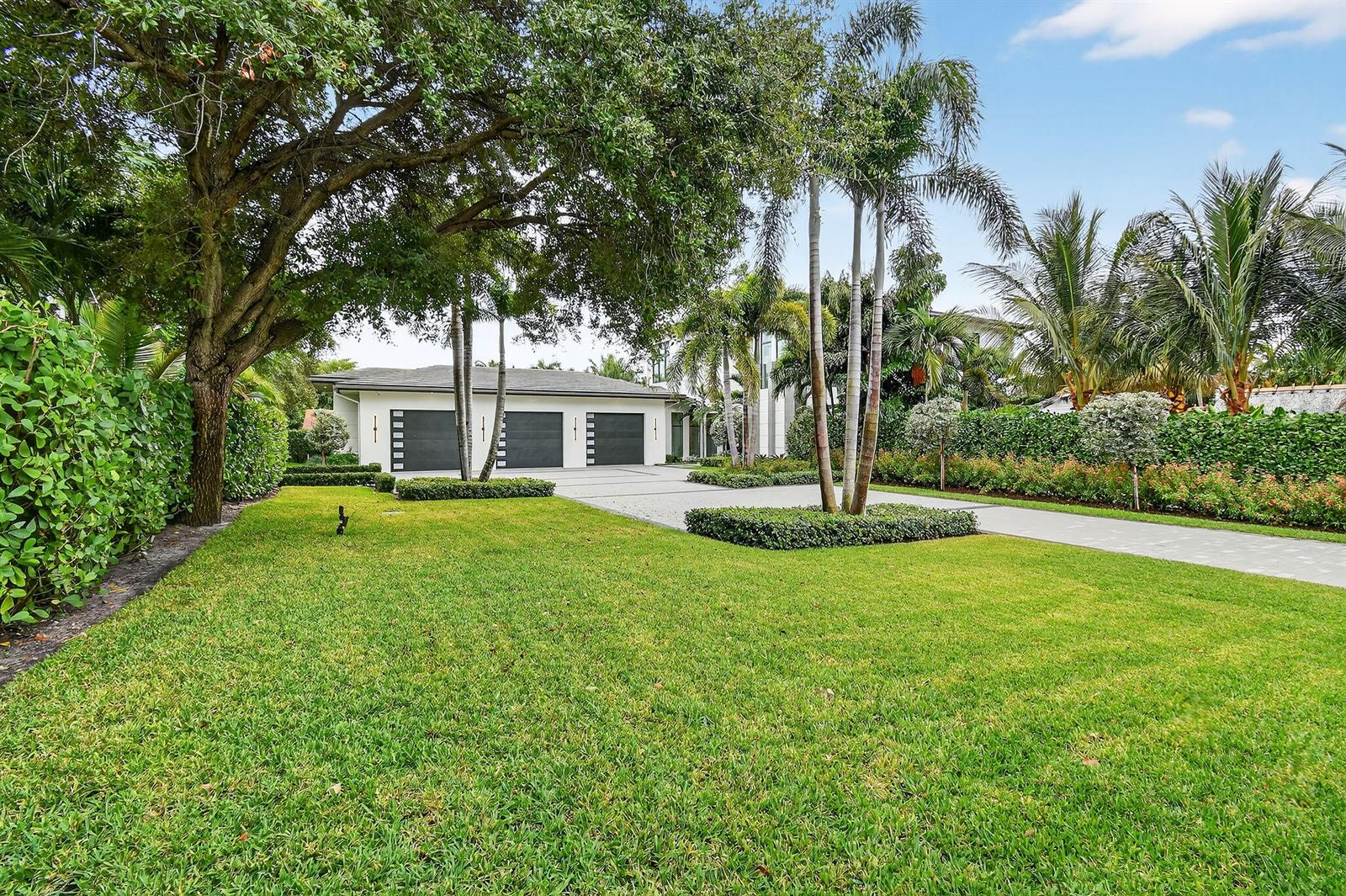 A three-car garage sits at the end of a paved driveway surrounded by lush landscaping — 2085 Vitex Lane, North Palm Beach FL 33408, NORTH PALM BEACH, FL