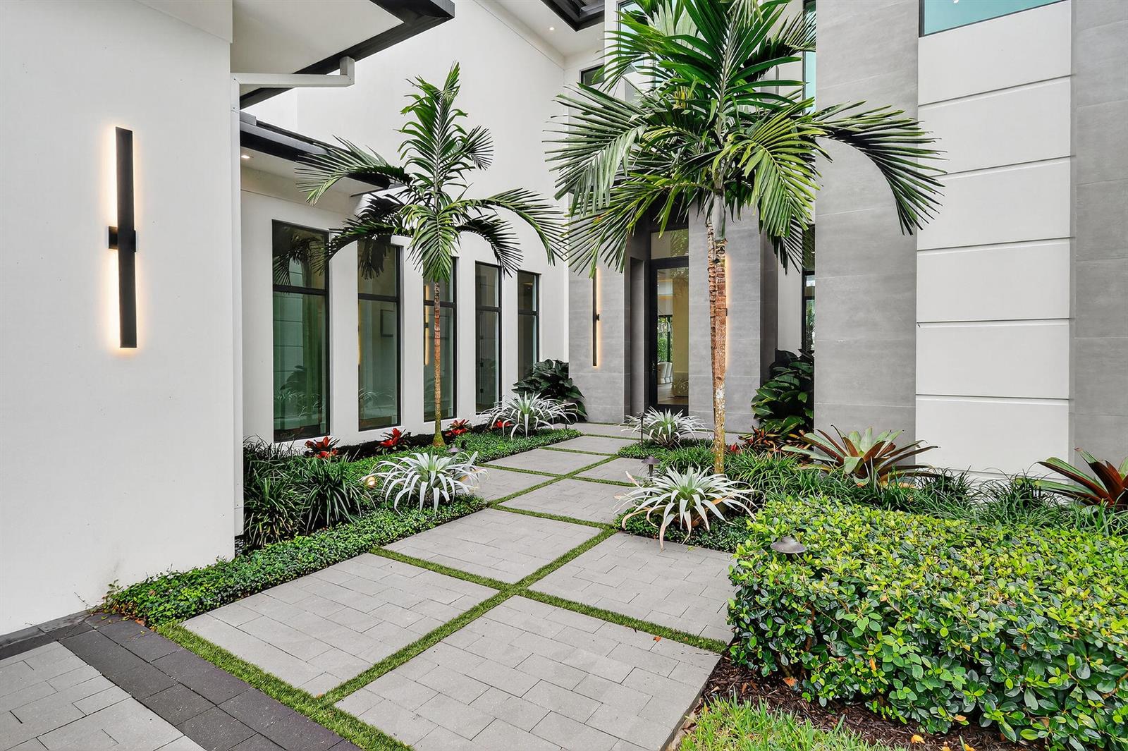 A modern home entrance features a paved walkway, palm trees, and manicured landscaping — 2085 Vitex Lane, North Palm Beach FL 33408, NORTH PALM BEACH, FL