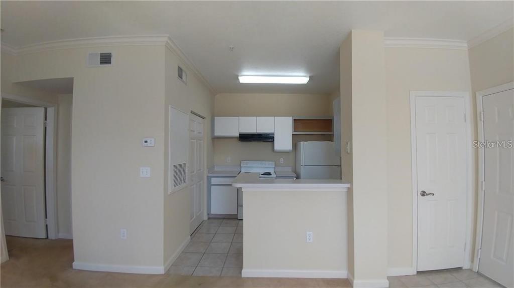 A kitchen with white cabinets, white appliances, and a breakfast bar opens to a hallway — 2652 ROBERT TRENT JONES DRIVE UNIT 534, ORLANDO, FL