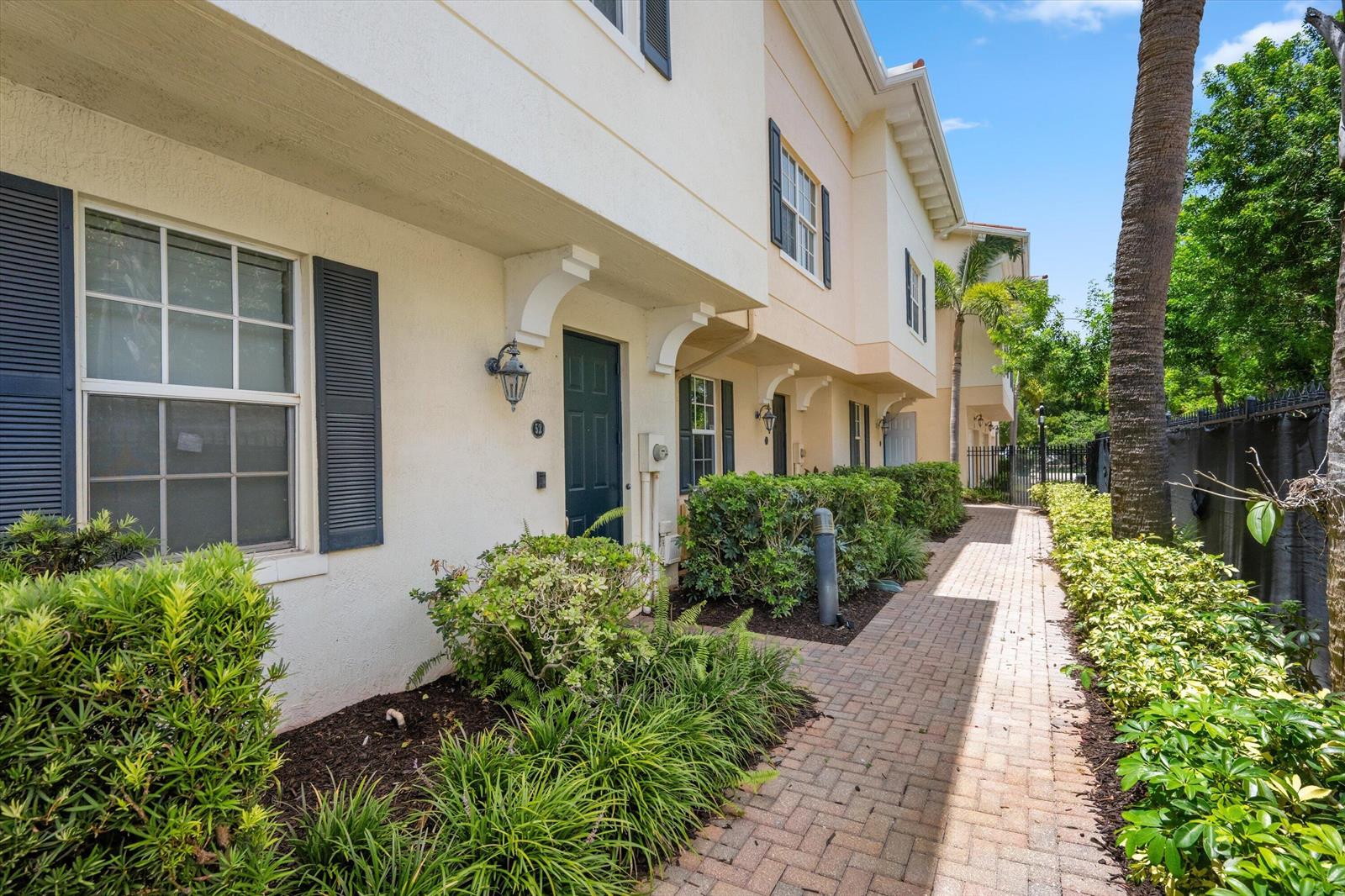 A brick walkway leads past townhome entrances with dark shutters and landscaping under a blue sky — 2502 N Dixie Highway # 52, FL 33460, FL