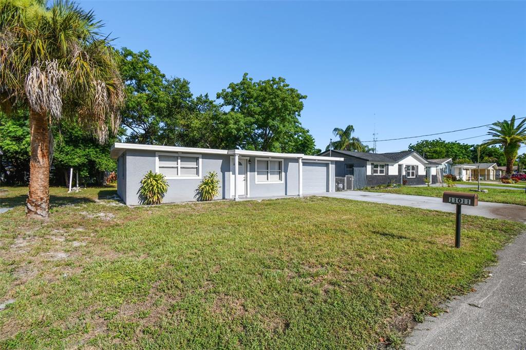 A single-story gray house with a flat roof, attached garage, and a front lawn — 11011 PICKERING LANE, PORT RICHEY, FL