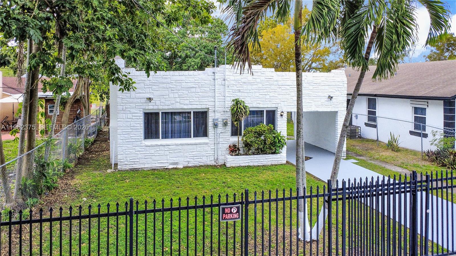 A white stone-textured house features a front lawn, a carport, and a black metal fence — 7770 NW 9th Ave, Miami FL 33150, MIAMI, FL