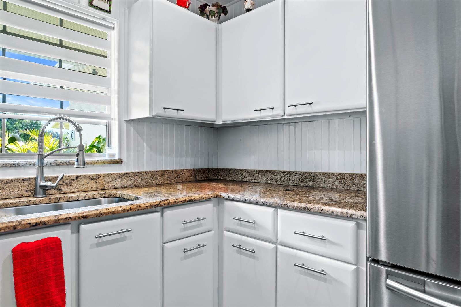 A kitchen features white cabinets, granite countertops, a stainless steel sink, and a stainless refrigerator — 5078 Lakefront Boulevard # D, Delray Beach FL 33484, DELRAY BEACH, FL