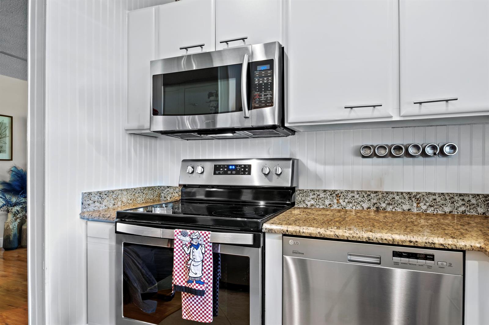 A kitchen features white cabinets, stainless steel appliances, and granite countertops with a beadboard backsplash — 5078 Lakefront Boulevard # D, Delray Beach FL 33484, DELRAY BEACH, FL