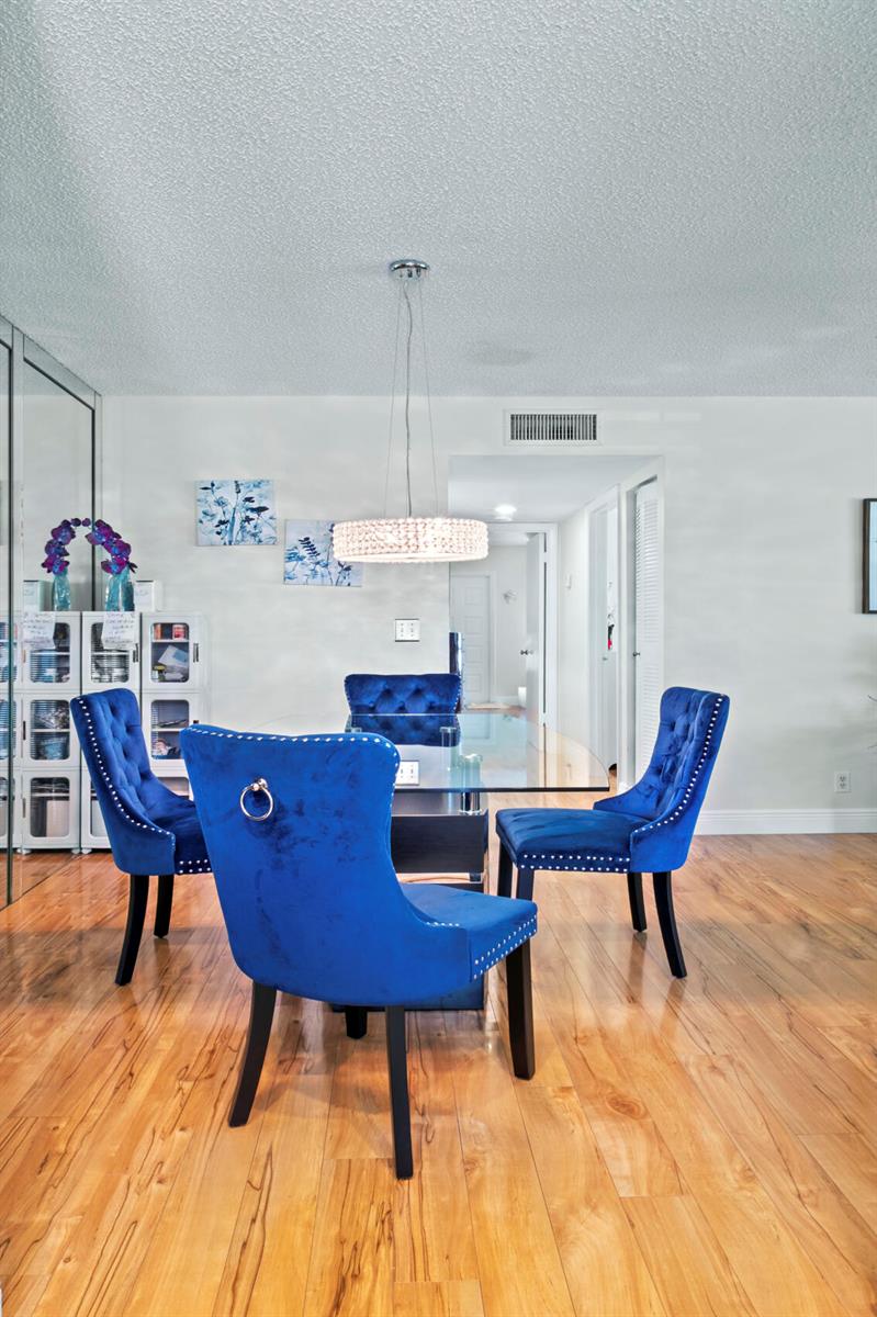 A dining room features a glass table, blue velvet chairs, and a crystal chandelier — 5078 Lakefront Boulevard # D, Delray Beach FL 33484, DELRAY BEACH, FL