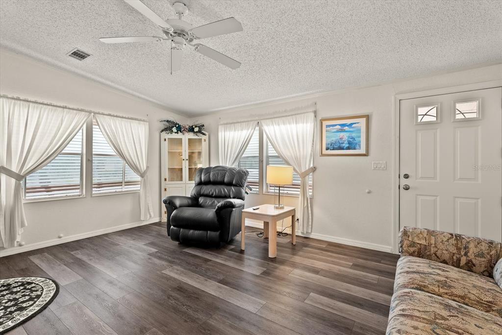A living room features wood-look flooring, a ceiling fan, a recliner, and a white door — 321 BLACKBURN BOULEVARD, NORTH PORT, FL