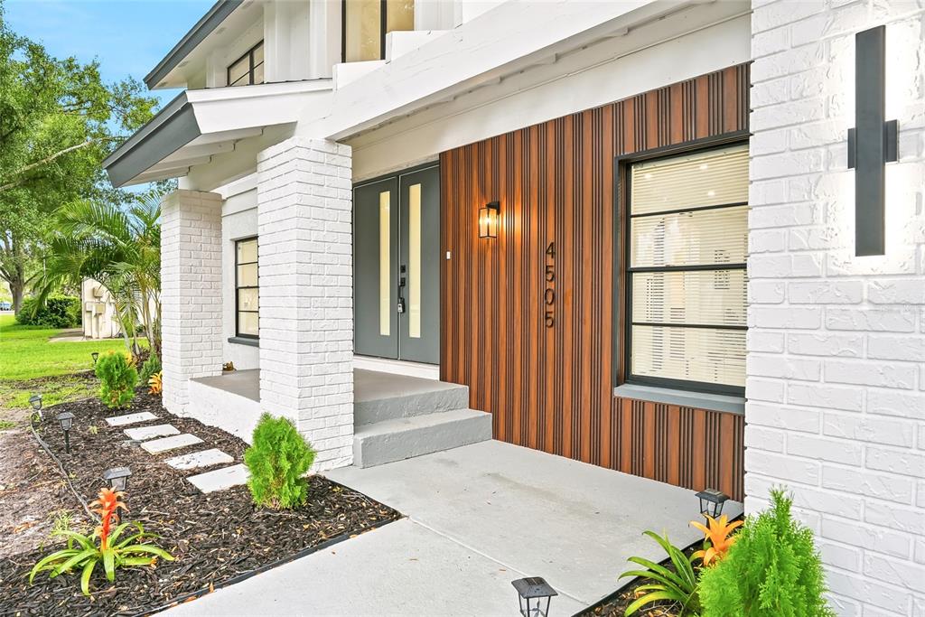The exterior of a house features white brick, wood-slat siding, a gray door, and landscaping — 4505 WHITWORTH LANE, TAMPA, FL