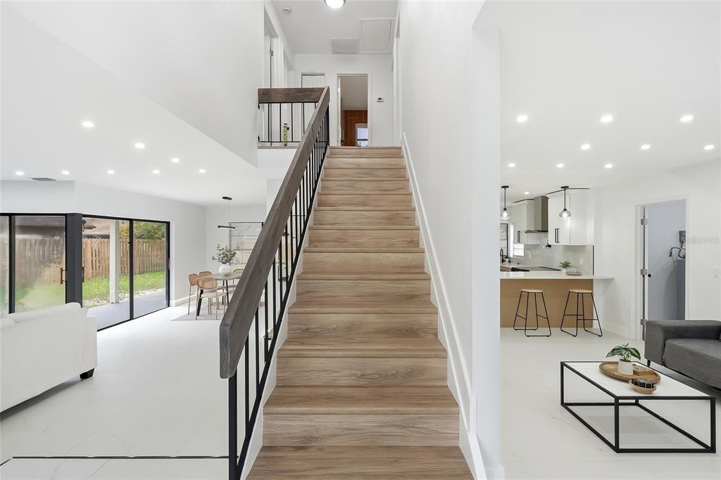 A central wooden staircase with black railings separates an open-concept living area and kitchen — 4505 WHITWORTH LANE, TAMPA, FL