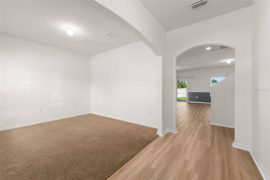 A carpeted room with an arched entryway leads to a living area with wood flooring — 8008 SW 62ND COURT, GAINESVILLE, FL