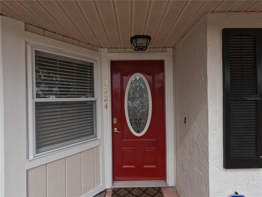 A red front door with an oval glass insert sits beside a window with blinds — 3924 CREWS LAKE DRIVE, LAKELAND, FL