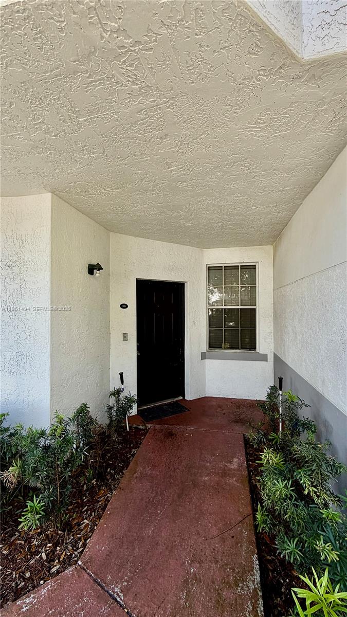A concrete walkway leads to the black front door of a stucco home exterior — 741 SW 148th Ave # 705, Sunrise FL 33325, SUNRISE, FL