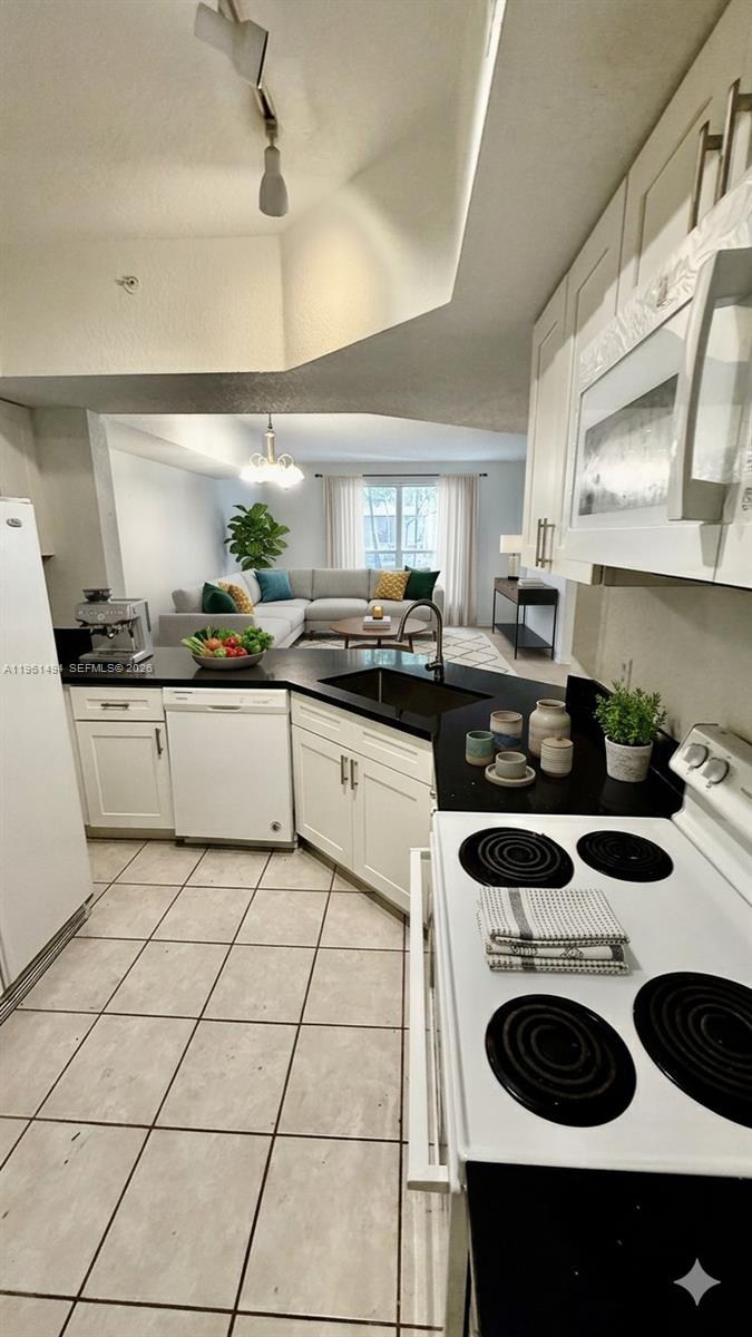 A kitchen with white cabinets and black countertops overlooks a living room with a sofa — 741 SW 148th Ave # 705, Sunrise FL 33325, SUNRISE, FL