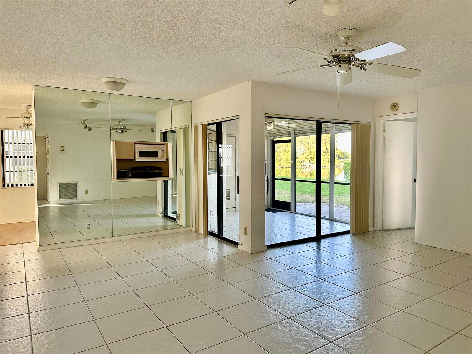A tiled living room features a mirrored wall, a ceiling fan, and a screened-in patio — 5819 Parkwalk Drive, Boynton Beach FL 33472, BOYNTON BEACH, FL