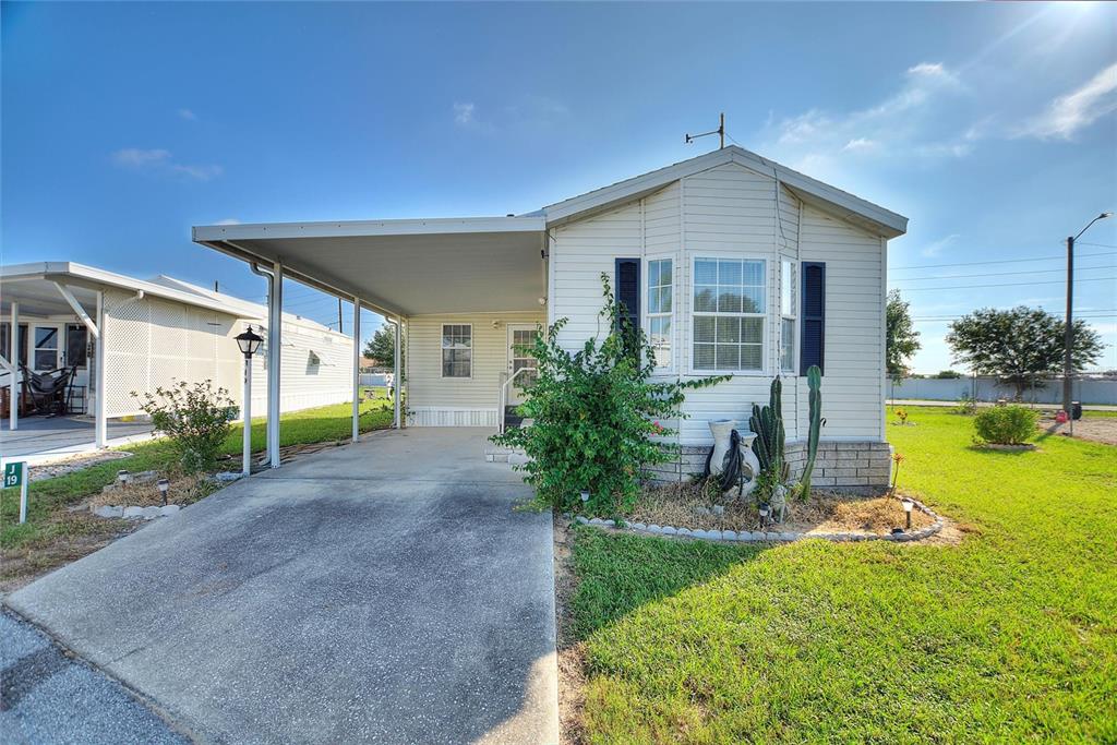 A single-story manufactured home with a carport, light siding, and a small front garden — 251 PATTERSON ROAD UNIT J19, HAINES CITY, FL