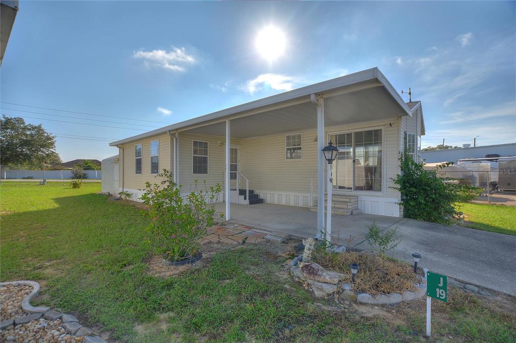 A light-yellow mobile home features a covered concrete carport and a small front yard — 251 PATTERSON ROAD UNIT J19, HAINES CITY, FL