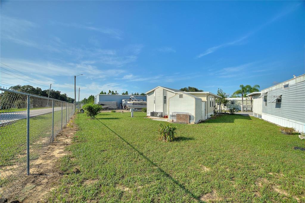 A light-colored mobile home with an attached shed sits on a grassy lot — 251 PATTERSON ROAD UNIT J19, HAINES CITY, FL