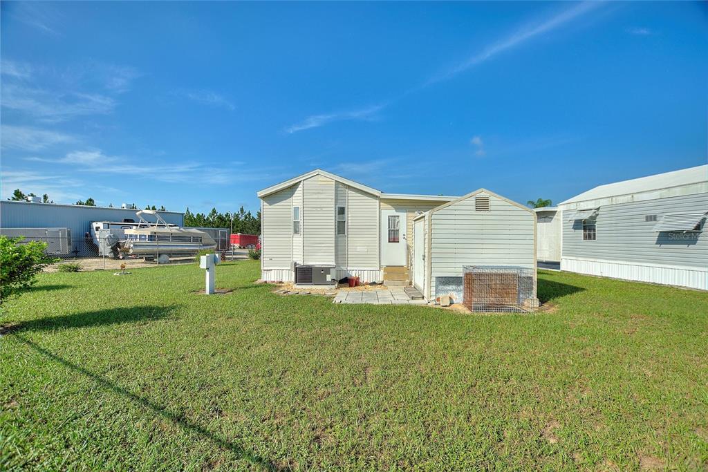 The exterior of a light-colored manufactured home sits on a grassy lot with trees — 251 PATTERSON ROAD UNIT J19, HAINES CITY, FL