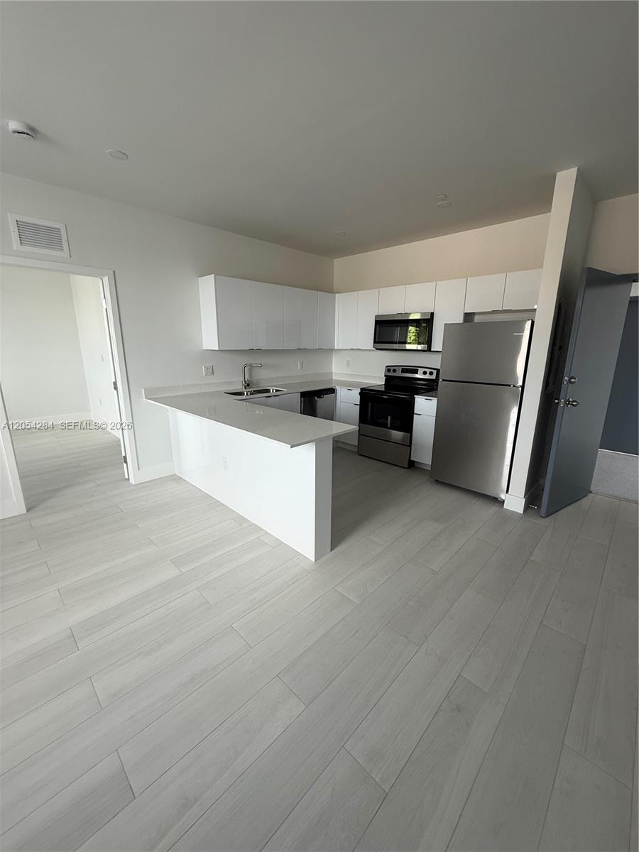 A modern kitchen features white cabinets, stainless steel appliances, and light wood-look flooring — 1091 E 17th St # 403, Hialeah FL 33010, HIALEAH, FL