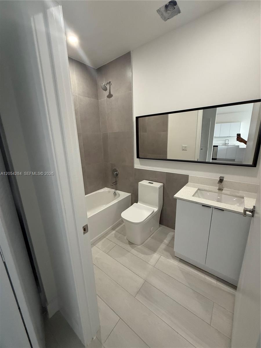 A modern bathroom features a white vanity, a toilet, and a tiled bathtub shower combination — 1091 E 17th St # 403, Hialeah FL 33010, HIALEAH, FL