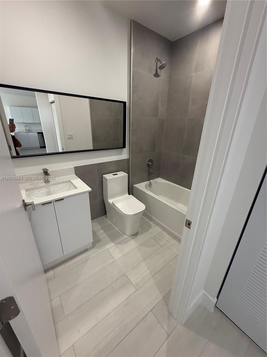 A modern bathroom features a white vanity, a toilet, and a tiled shower-tub combination — 1091 E 17th St # 403, Hialeah FL 33010, HIALEAH, FL